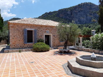 A stone house, which has with a tiled courtyard, a fountain, and an olive tree, with a view of the mountain